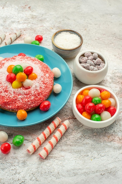 無料写真 正面図白い背景の上のカラフルなキャンディーとおいしいピンクのケーキデザートカラーグッディレインボーケーキキャンディー