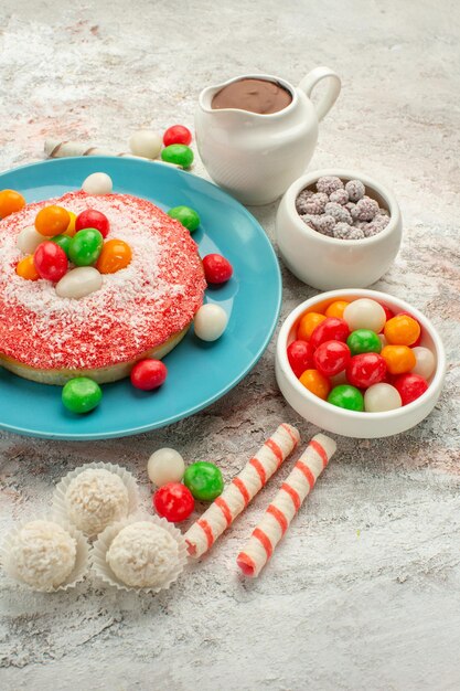 Front view delicious pink cake with colorful candies on a white background dessert color rainbow candy cake goodie