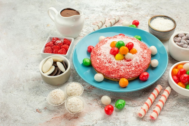 正面図白い背景の上のカラフルなキャンディーとおいしいピンクのケーキデザートグッディレインボーカラーケーキキャンディー