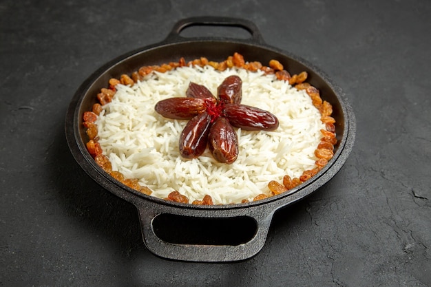 Vista frontale deliziosa farina di riso cotta plov con uvetta all'interno di una padella sulla superficie scura cibo riso cena orientale