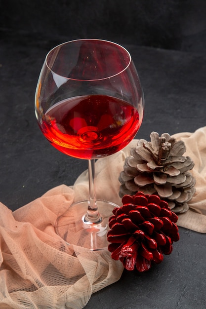 Front view of delicious red wine in a glass goblet on towel and conifer cones on a dark background