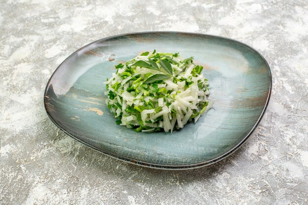 Вкусный салат вид спереди состоит из зелени и капусты внутри тарелки на белой поверхности