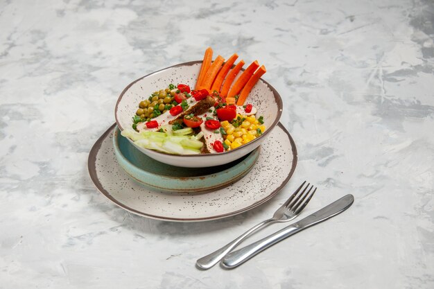 Вид спереди вкусного салата с различными ингредиентами на тарелке на подносах и набором столовых приборов на белой поверхности со свободным пространством