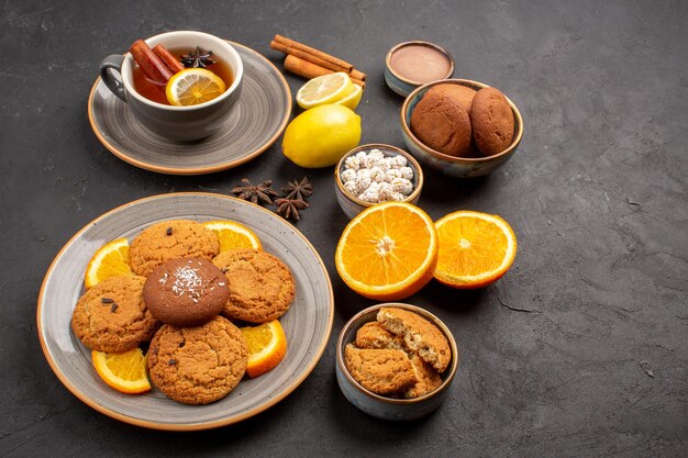 Front view delicious sand cookies with fresh oranges and cup of tea on dark background fruit biscuit sweet cookie citrus sugar