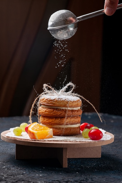 Front view delicious sandwich cookies tied yummy with sliced fruits and sugar powder on the dark-blue desk cake 