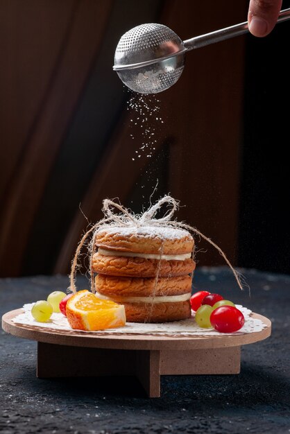 Front view delicious sandwich cookies tied yummy with sliced fruits and sugar powder on the dark-blue desk cake 