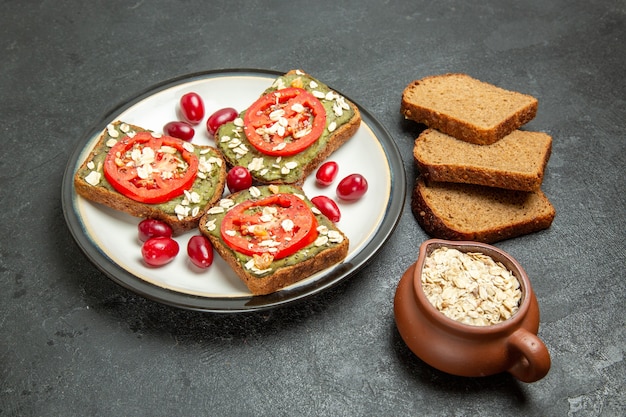 Вид спереди вкусные бутерброды с пастой авокадо и помидорами внутри тарелки на темно-сером фоне, булочка с гамбургером, закуска, хлеб