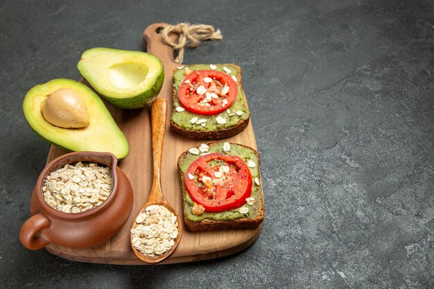 Вид спереди вкусные бутерброды с авокадо и красными помидорами на сером фоне обед закуска гамбургер сэндвич еда