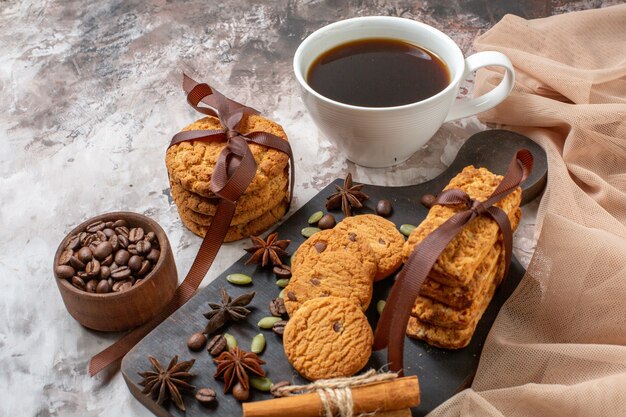 Front view delicious sweet biscuits with coffee seeds and cup of coffee on a light cocoa sugar tea cookie sweet cake color