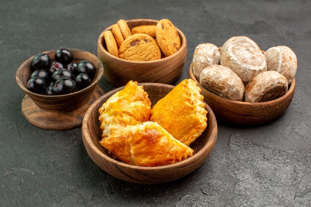 Вид спереди вкусные сладкие пирожные с печеньем и оливками на темной поверхности сладкого пирога