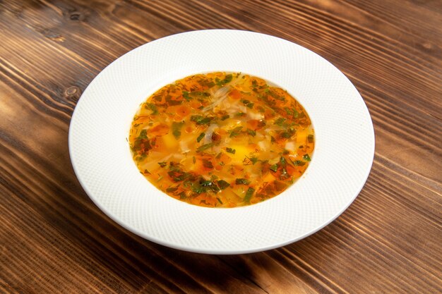 Вид спереди вкусный овощной суп с зеленью на коричневом деревянном столе суп овощная еда приправы