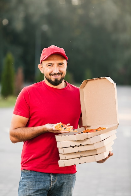 Front view delivery guy holding a pizza slice