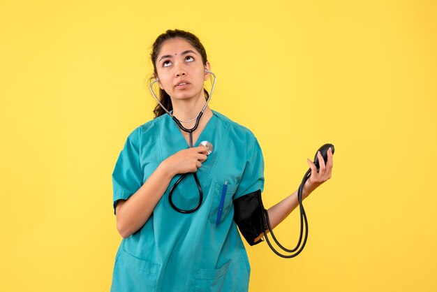 正面図は、黄色の背景で高く見える血圧計を保持している制服を着た女性医師を決定しました