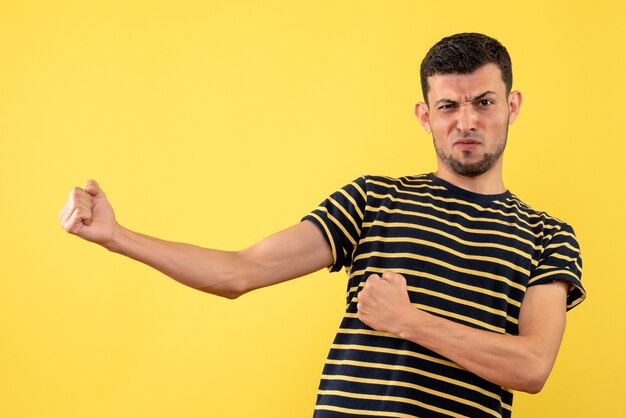 Front view determined young man in black and white striped t-shirt yellow isolated background