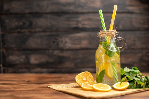 Front view of detox water made of lemon and mint on an old newspaper on the left side on brown wooden background