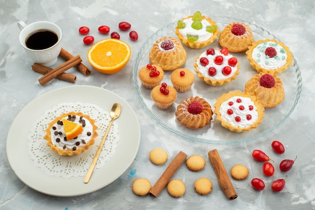 Front view different cakes with cookies cinnamon and cup of coffee on the light surface sugar sweet fruit