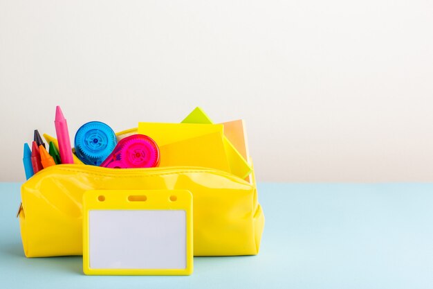 Front view different colorful pencils inside yellow pen box on the blue desk