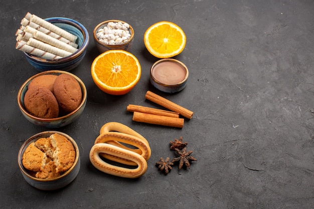 Front view different cookies with sliced oranges on dark background sugar tea biscuit cookie sweet fruit