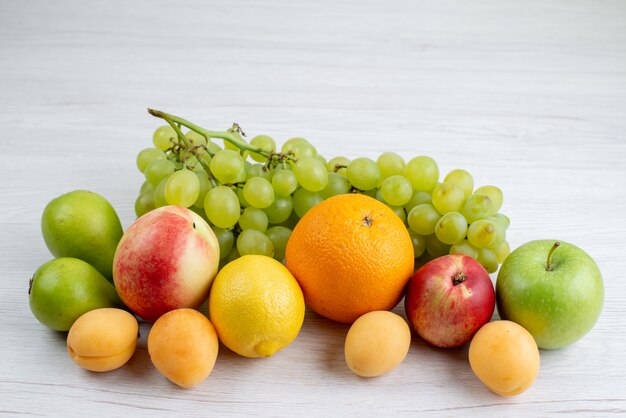 A front view different fruits mellow and fresh fruits such as apricots grapes apples on the white desk fruit composition color vitamine