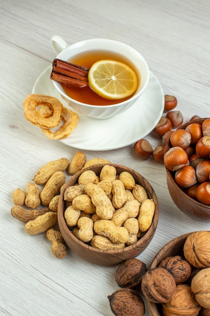 Front view different nuts peanuts hazelnuts and walnuts with cup of tea on white surface