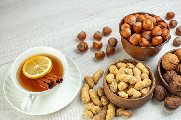 Front view different nuts peanuts hazelnuts and walnuts with cup of tea on white surface