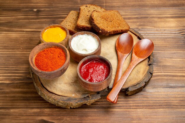 Front view different seasonings with dark bread loafs on a brown desk bread spicy seasoning