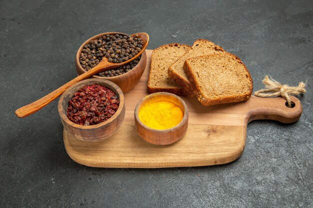 Front view different seasonings with dark bread loafs on dark grey background bread bun spicy hot seasoning