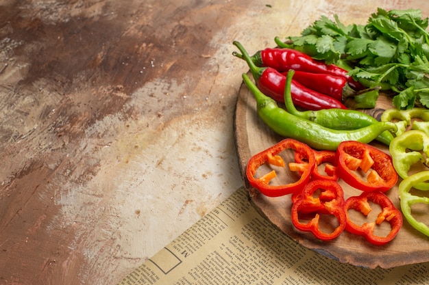 Front view different vegetables coriander hot peppers bell peppers cut into pieces on round tree wood board