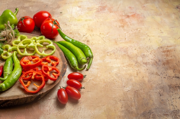 Front view different vegetables hot peppers bell peppers cut into pieces on round tree wood board cherry tomatoes peppers on yellow ochre background