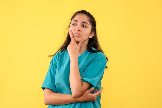 Front view disappointed female doctor in uniform putting hand on her chin on yellow isolated background