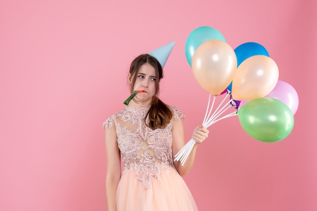 Free photo front view disappointed party girl with party cap holding balloons using noisemaker