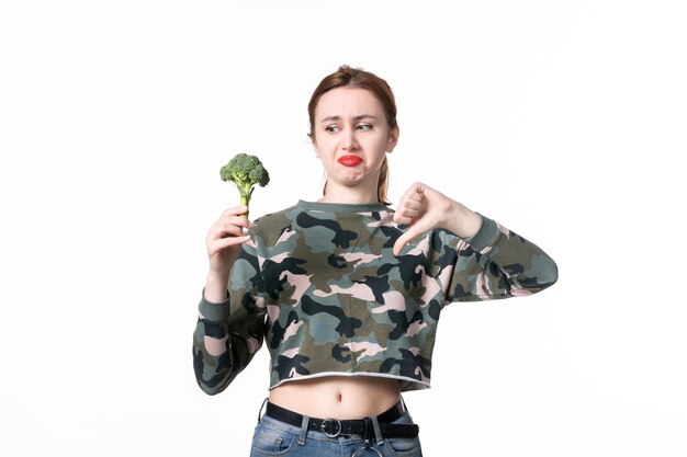 Front view displeased young female holding little broccoli on white