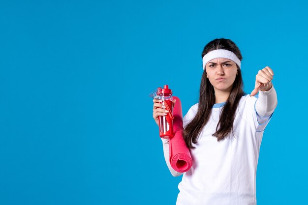 Front view displeased young female with carpet for exercises and bottle of water