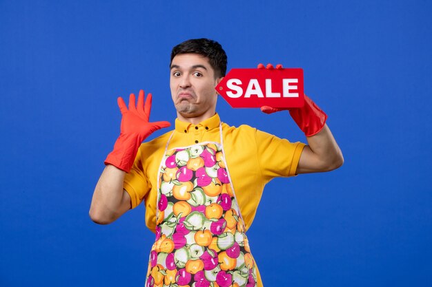 Front view dissatisfied male housekeeper with red drain gloves holding sale sign on blue space