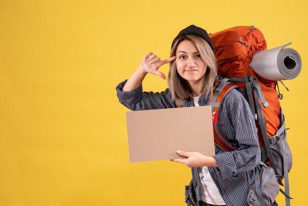 Front view of dissatisfied traveler woman with backpack holding cardboard