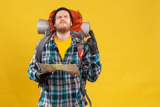 Front view of dissatisfied young backpacker with leather gloves holding map