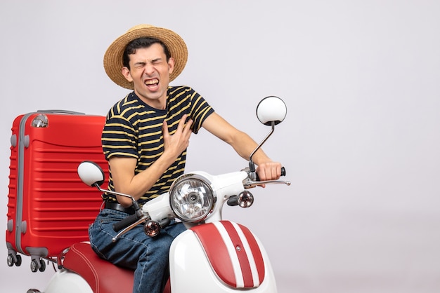 Front view of dissatisfied young man with straw hat on moped holding his heart