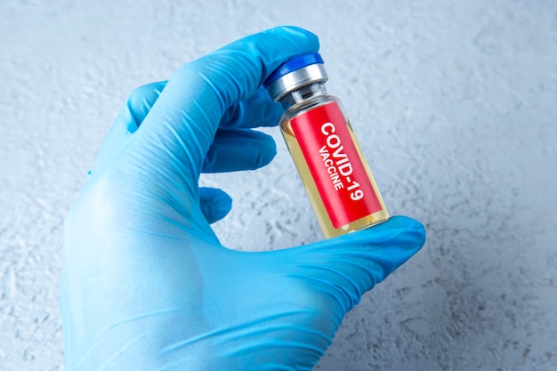 Front view of doctor hand holding covid- vaccine ampoule on gray sand background