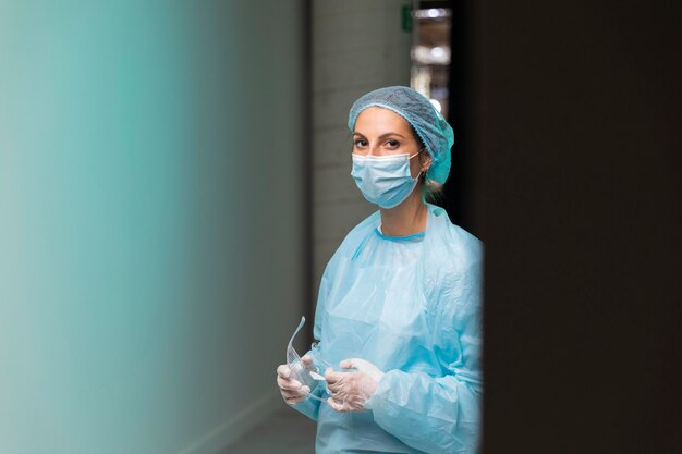 Front view doctor in protective wear holding her goggles