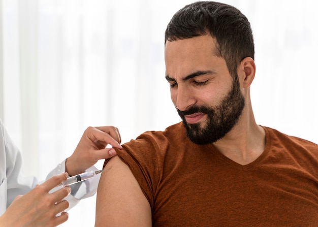 Вид спереди врача, вакцинирующего бородатого мужчину