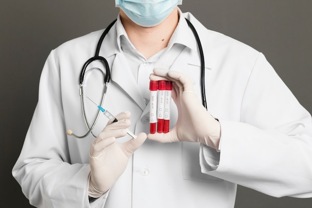 Foto gratuita vista frontale del medico con maschera medica tenendo la siringa e vacutainer