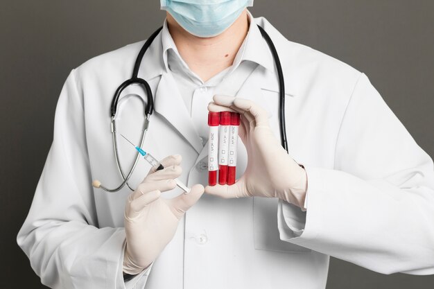 Front view of doctor with medical mask holding syringe and vacutainers