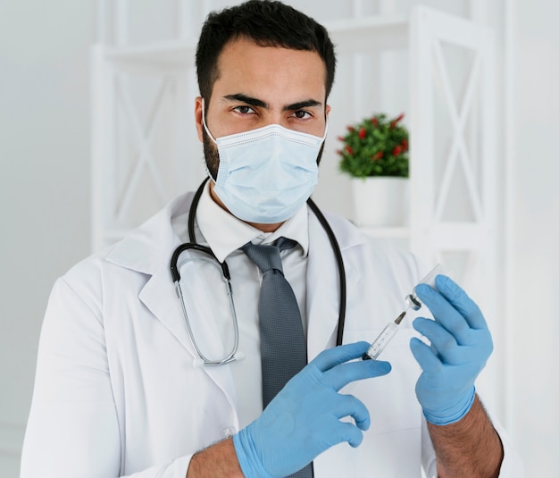 Front view doctor with medical mask holding a syringe