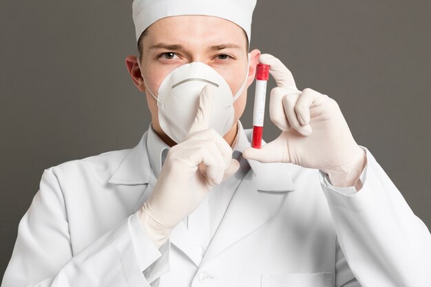 Front view of doctor with medical mask holding up vacutainer and making the quiet sign