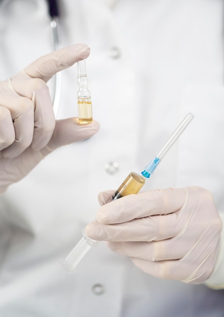 Front view of doctor with surgical gloves holding medication and syringe