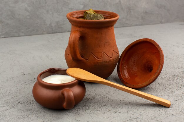 front view dolma along with yogurt inside brown pots on the grey floor