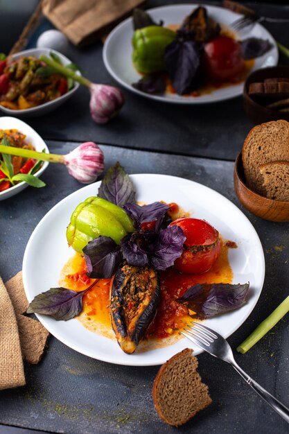 A front view dolma with minced meat inside vegetables oil inside white plate along with bread loafs flowers on the grey table beef dish