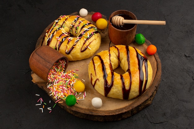 front view donuts with chocolate and colorful candies on the brown desk and grey