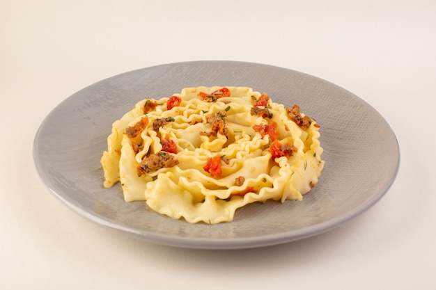 A front view dough pasta with cooked sliced vegetables and meat inside grey plate on white