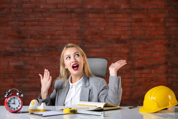 Front view dreaming female engineer sitting behind her working place